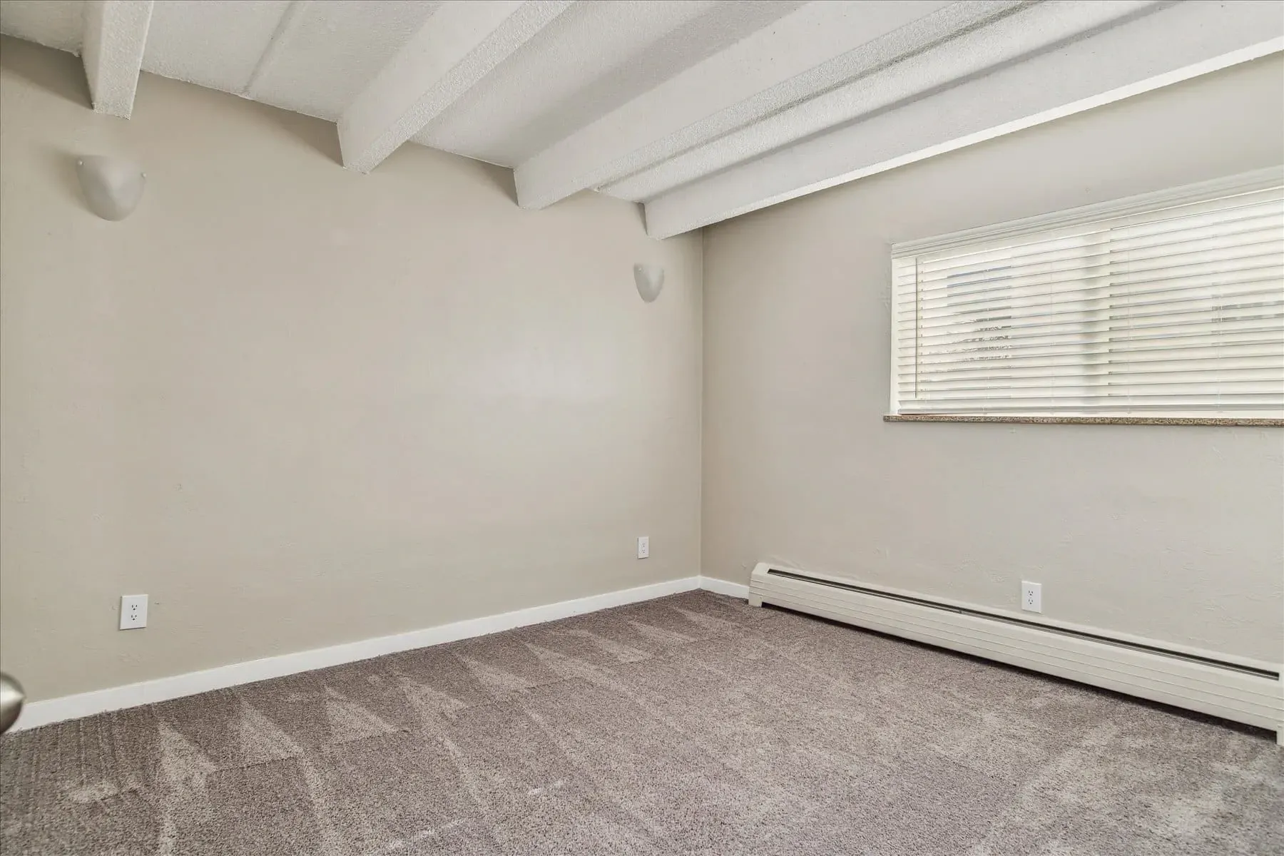 Empty bedroom with beige walls, carpeted floor, and a window with blinds.
