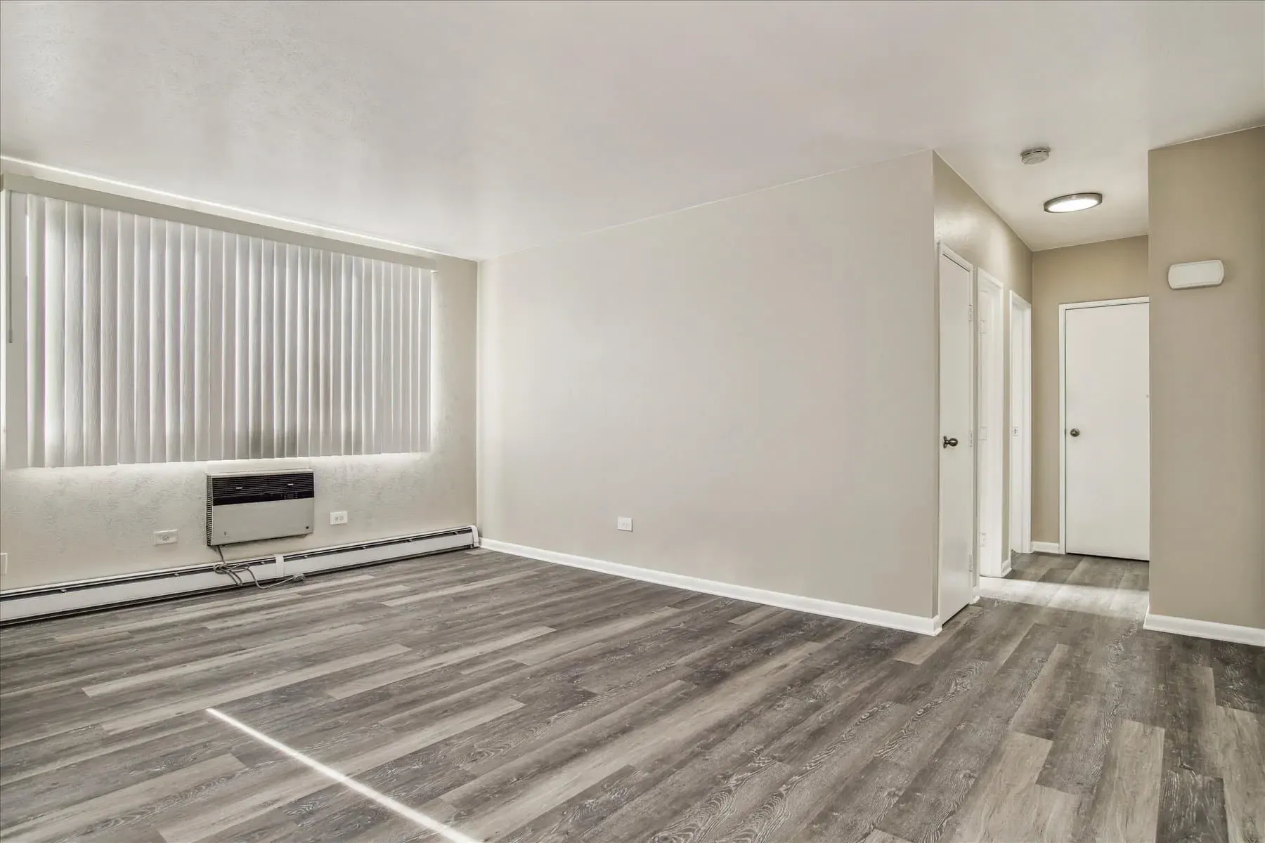 Empty living room with wood-look flooring and a large window.