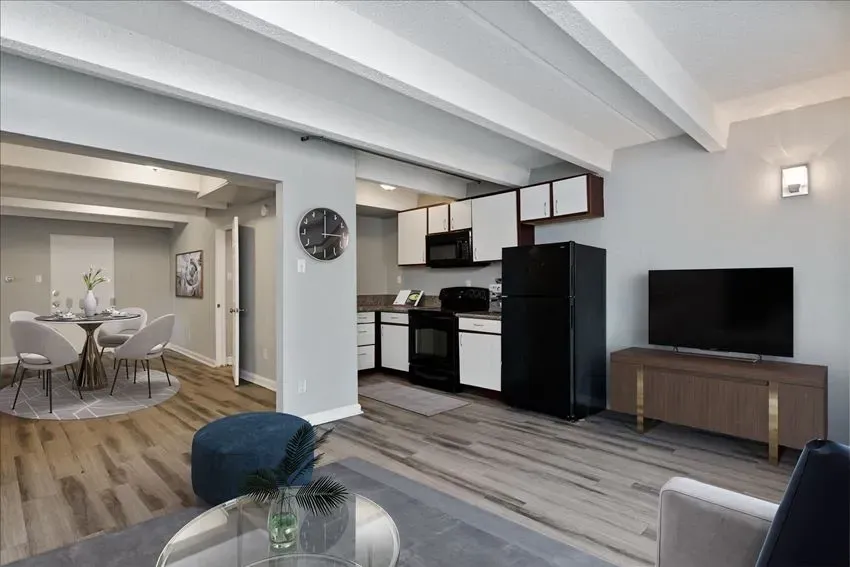 Modern apartment kitchen and living area with dining table, black refrigerator, and TV.