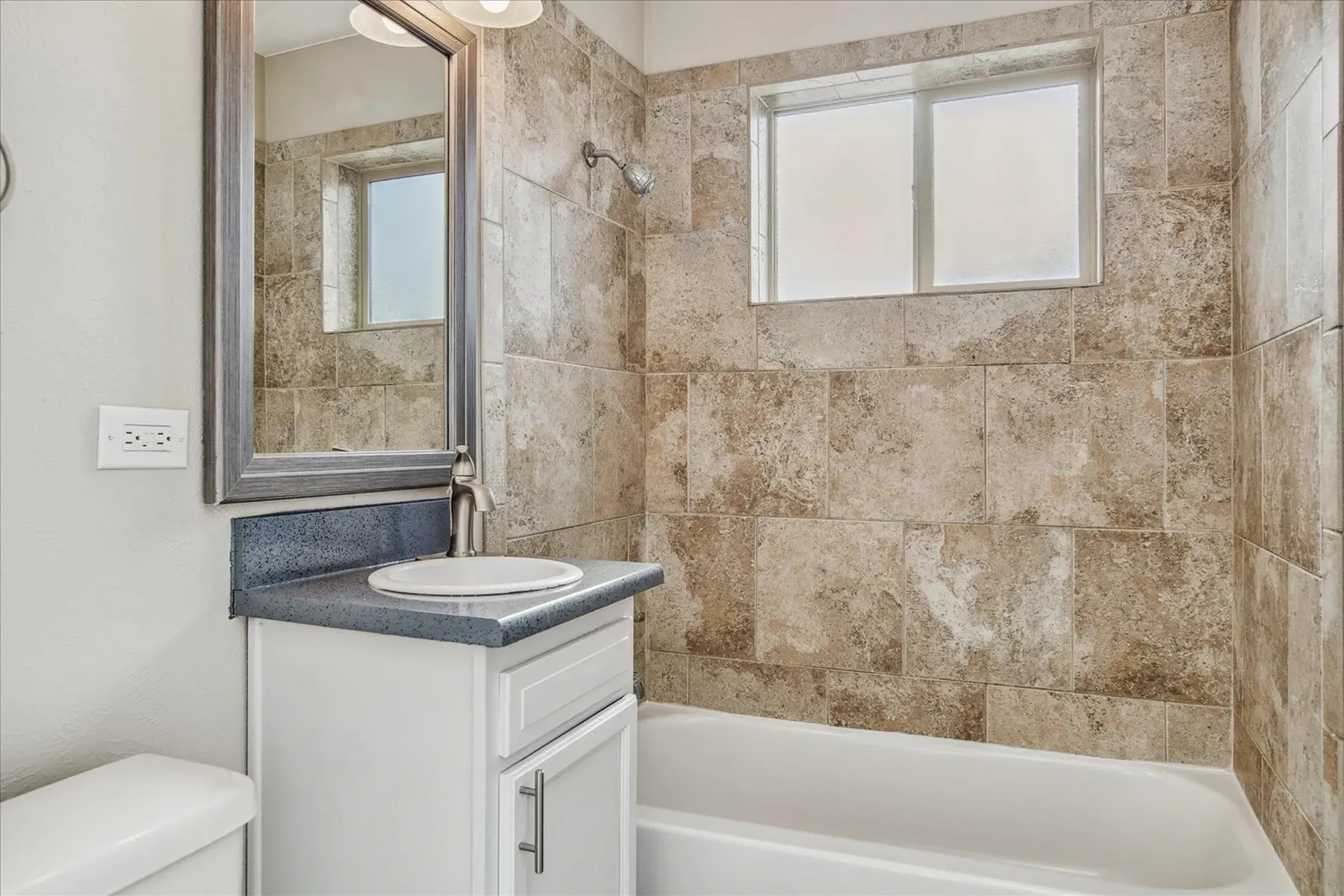 Bathroom with vanity, sink, mirror, and bathtub with tiled shower walls.