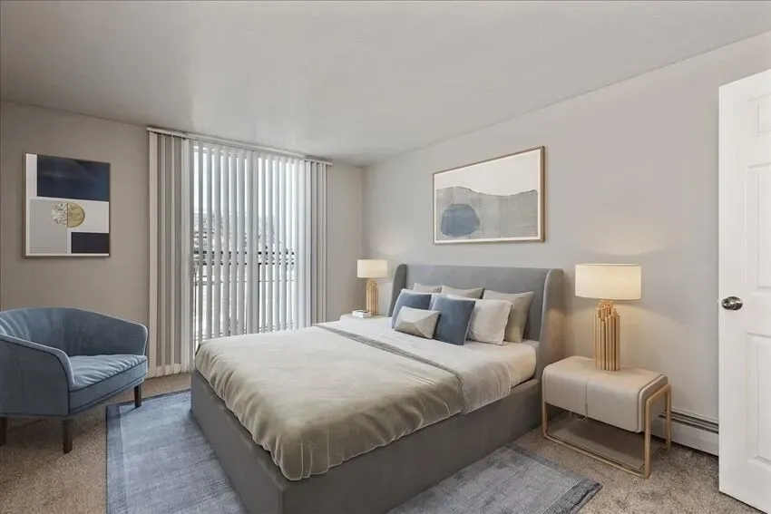 A beautifully staged bedroom with a king-size bed, a blue accent chair, and large windows.