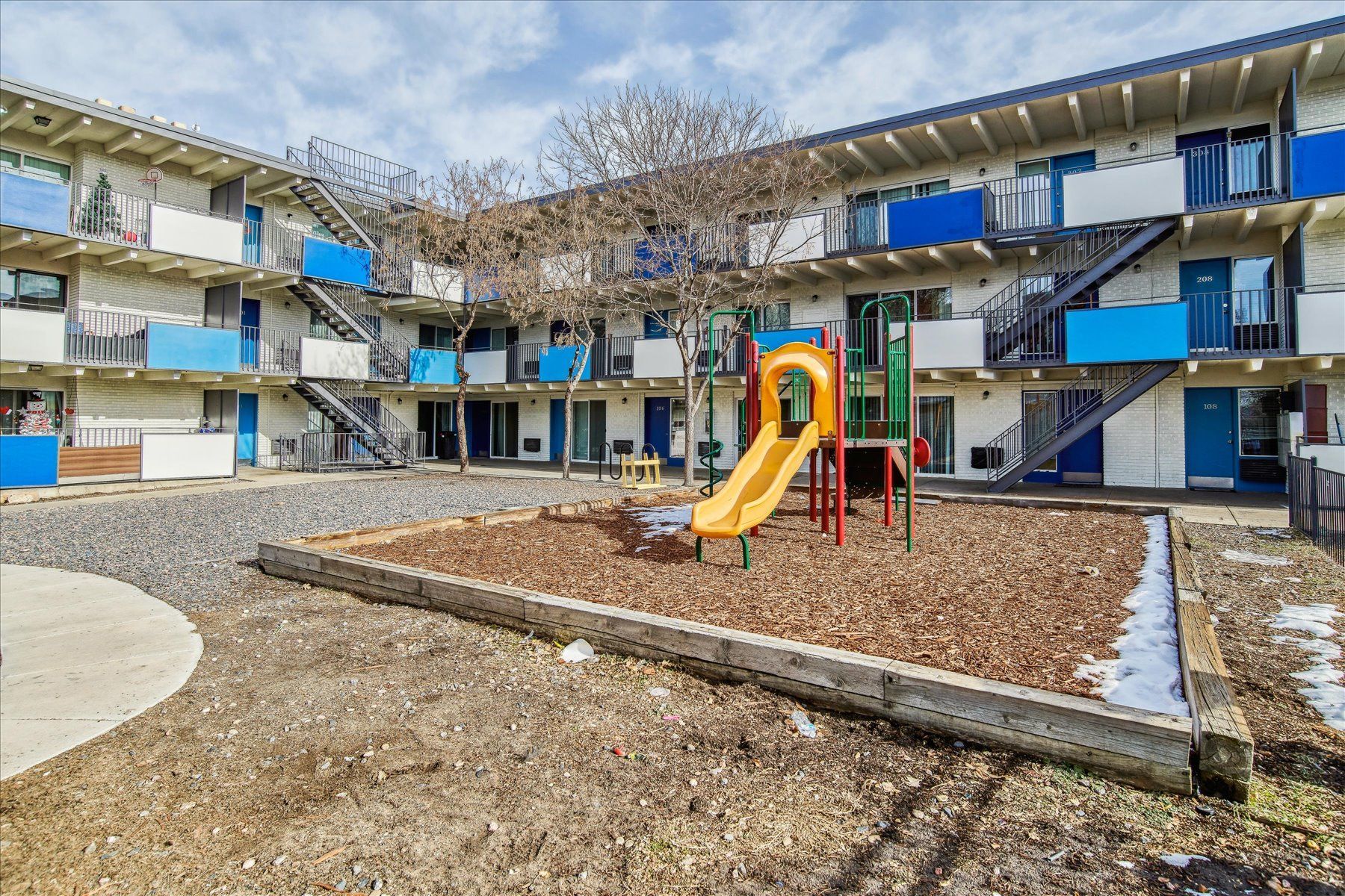 Apartment courtyard with a small playground, yellow slide, and blue balconies around the building