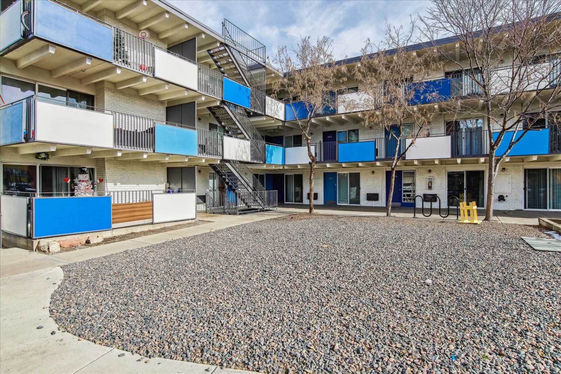 Apartment courtyard with gravel ground, beige balconies, and blue privacy panels