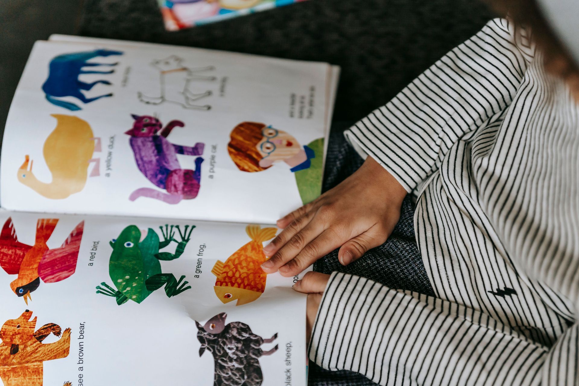 Person pointing at colorful animal illustrations in an open book