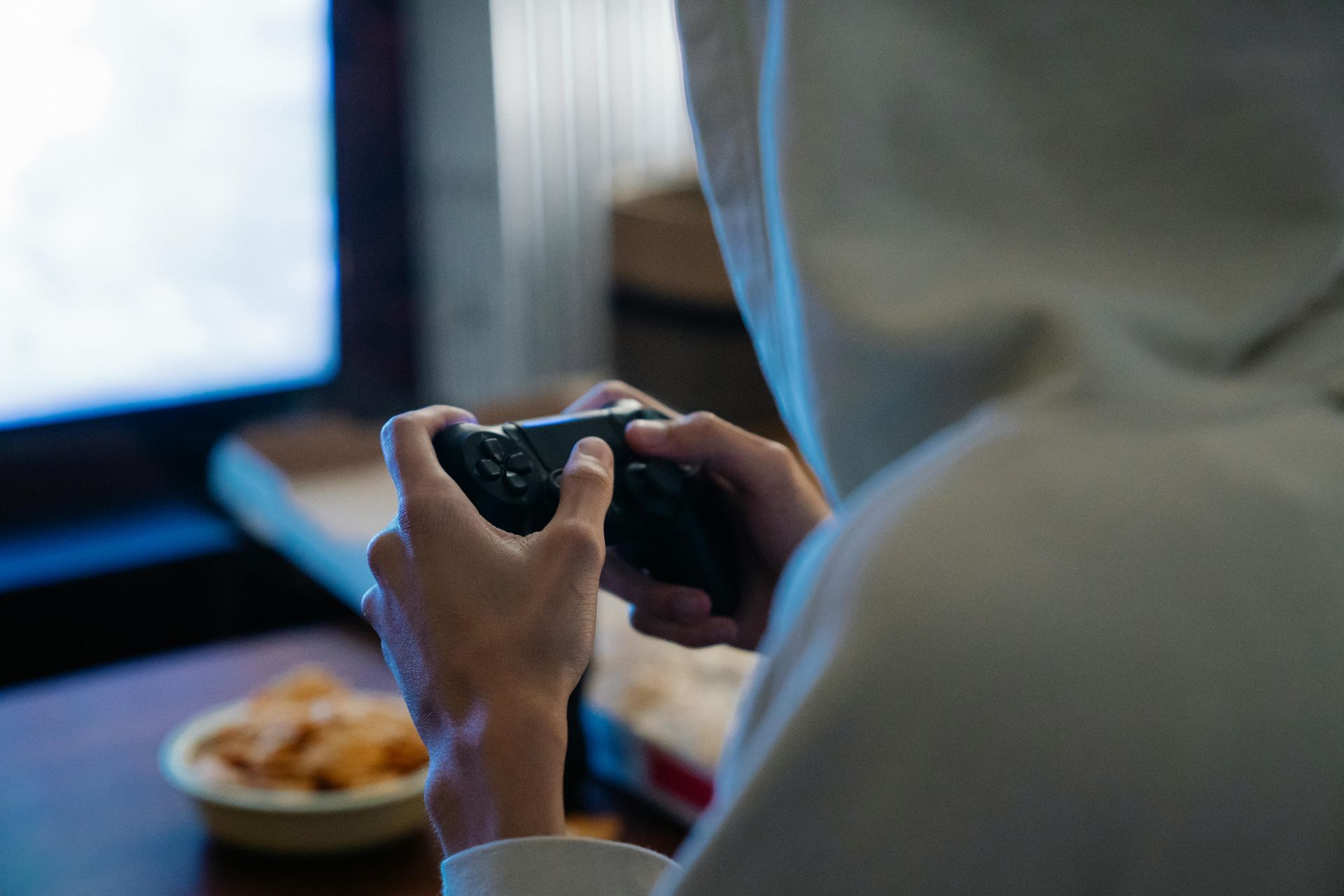 Teen holding a game controller in front of a TV with a bowl of snacks nearby