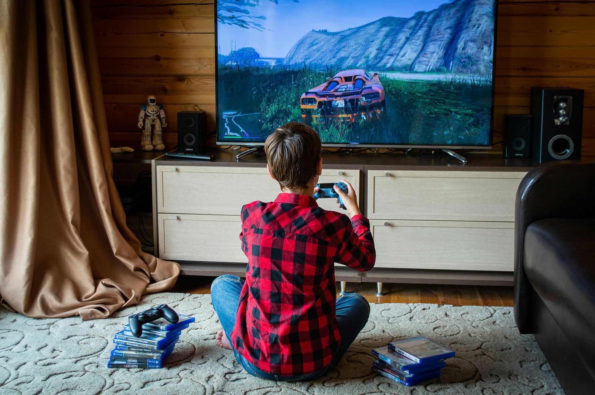 Person sits on rug gaming in front of a TV showing a car racing game in a cozy living room