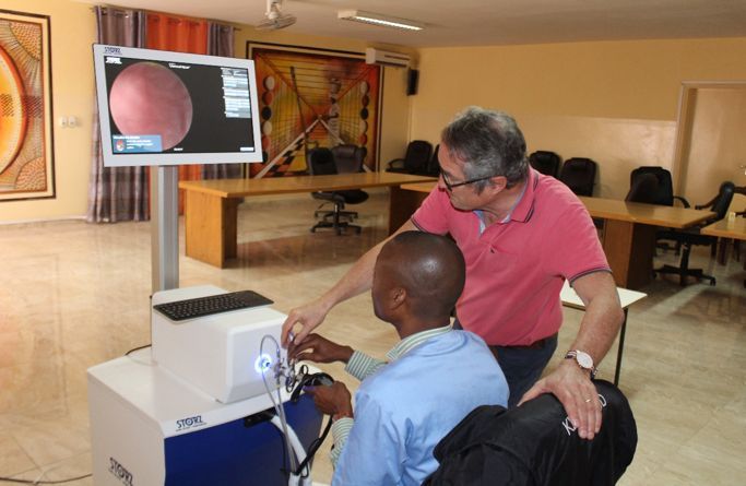 A man in a pink shirt is teaching another man how to use a computer