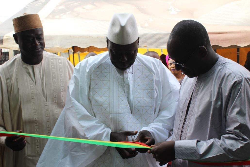Three men in white shirts are cutting a green ribbon