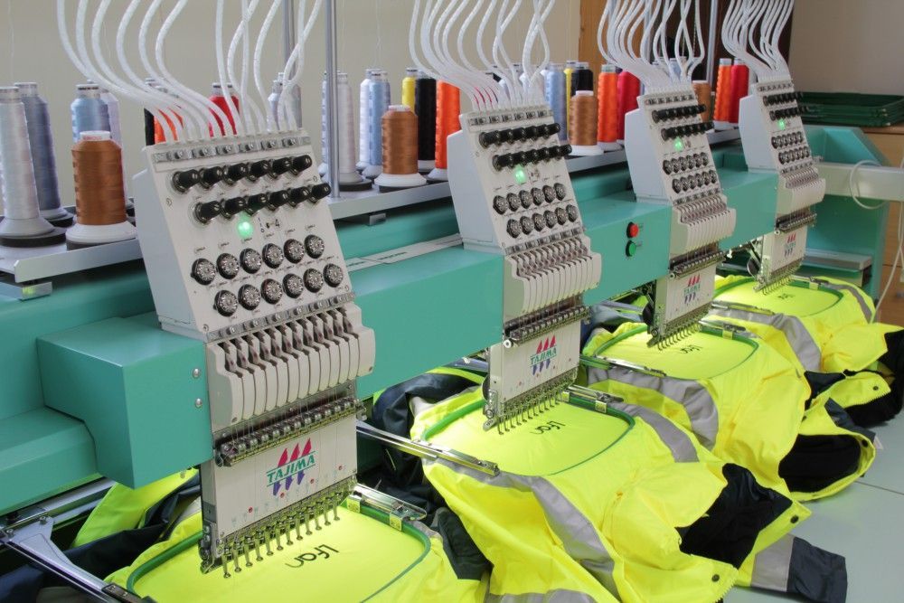 Une rangée de gilets jaunes est en train d'être brodée sur une machine.