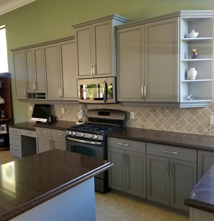 A modern kitchen with grey cabinets, dark countertops, a gas range, and a tiled backsplash.