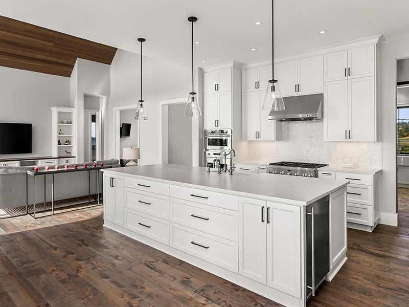 Modern kitchen with a large white island, white cabinetry, stainless steel appliances, and wood floors.