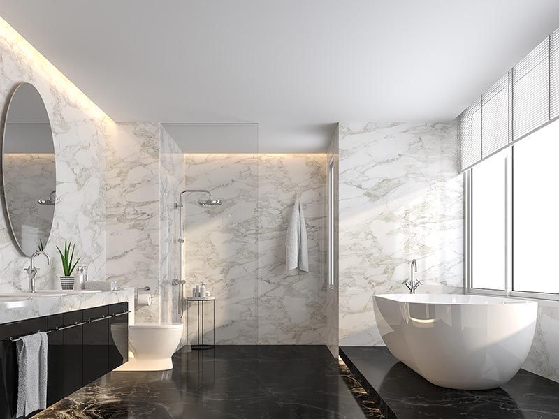 Modern luxury bathroom with white marble walls, black vanity and flooring, oval mirror, and walk-in shower.