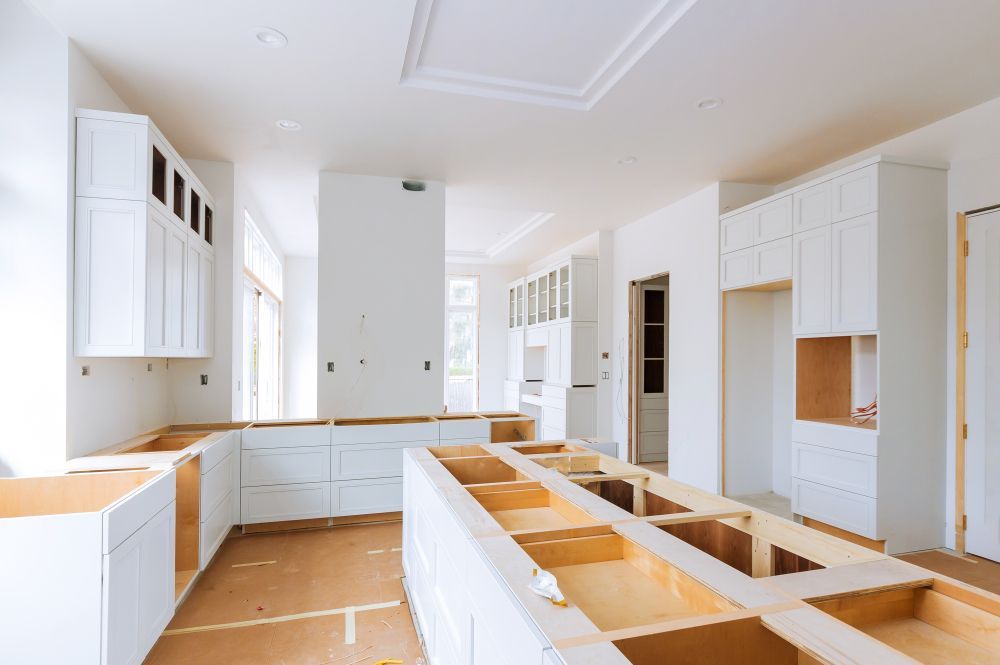 An unfinished kitchen with white cabinetry installed, a large island base, and exposed plywood surfaces.