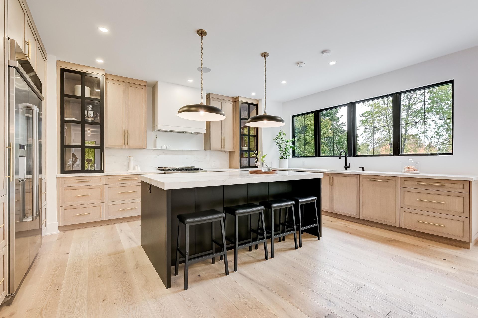 Modern kitchen with a dark center island, wooden cabinets, white countertops, black-framed windows, and two pendant lights.