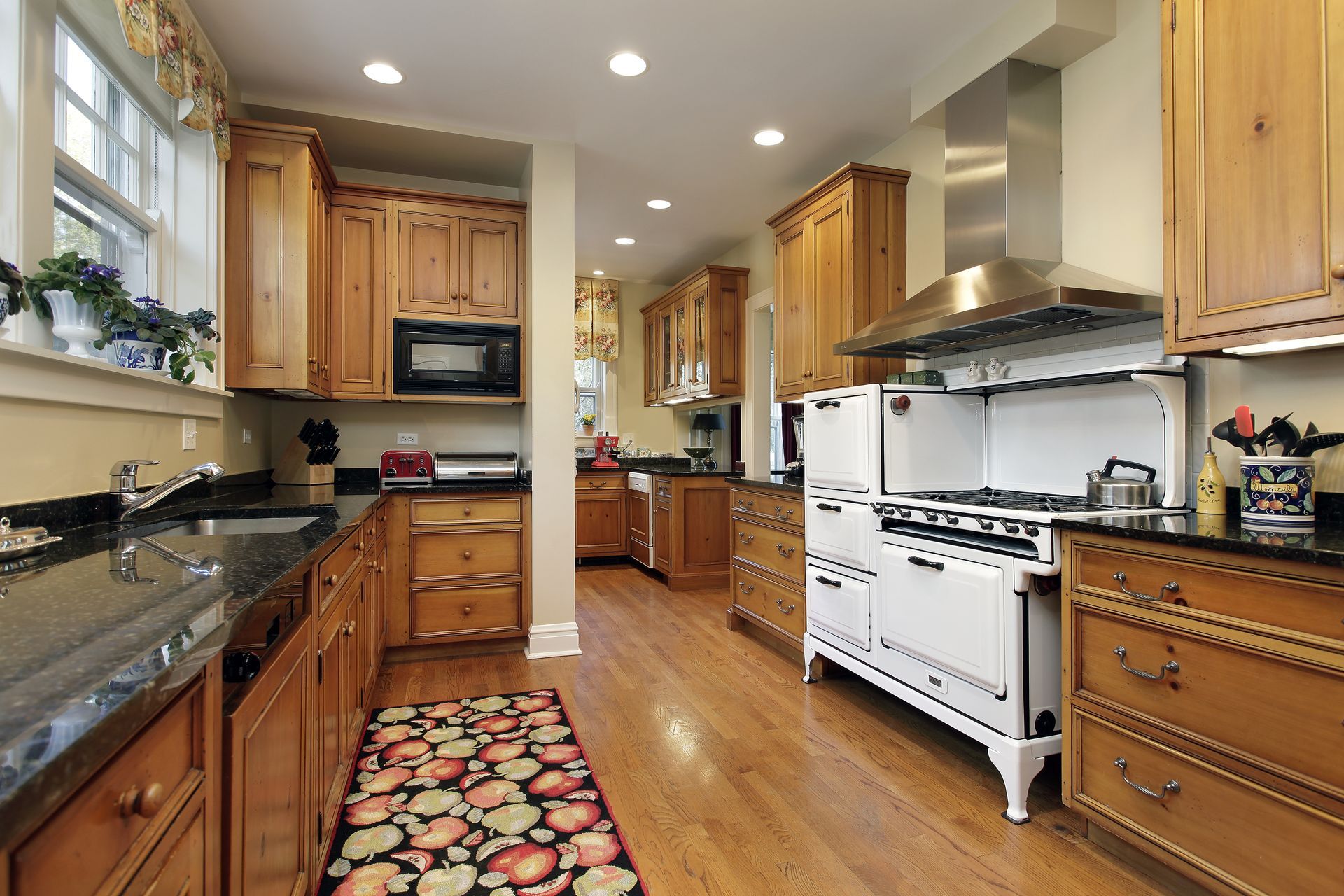 A rustic kitchen with wood cabinets, black countertops, a white vintage-style range, and an apple-patterned runner rug.