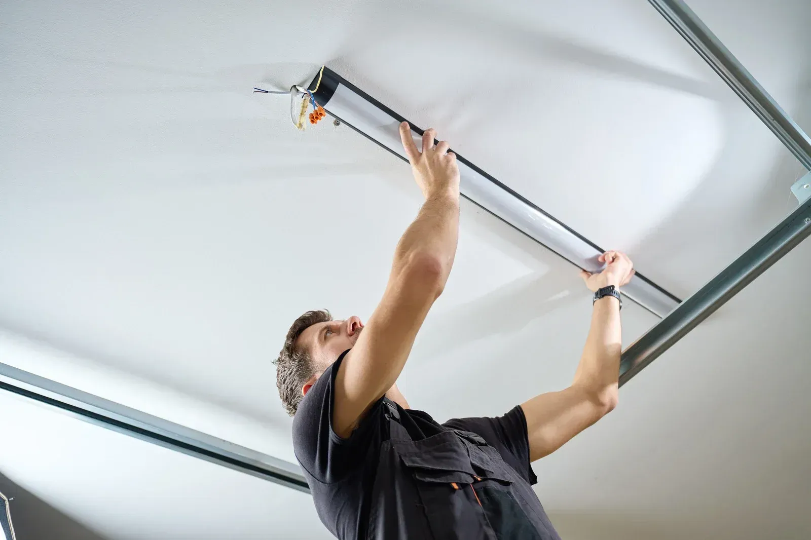 Person installing a fluorescent light fixture on a white ceiling.