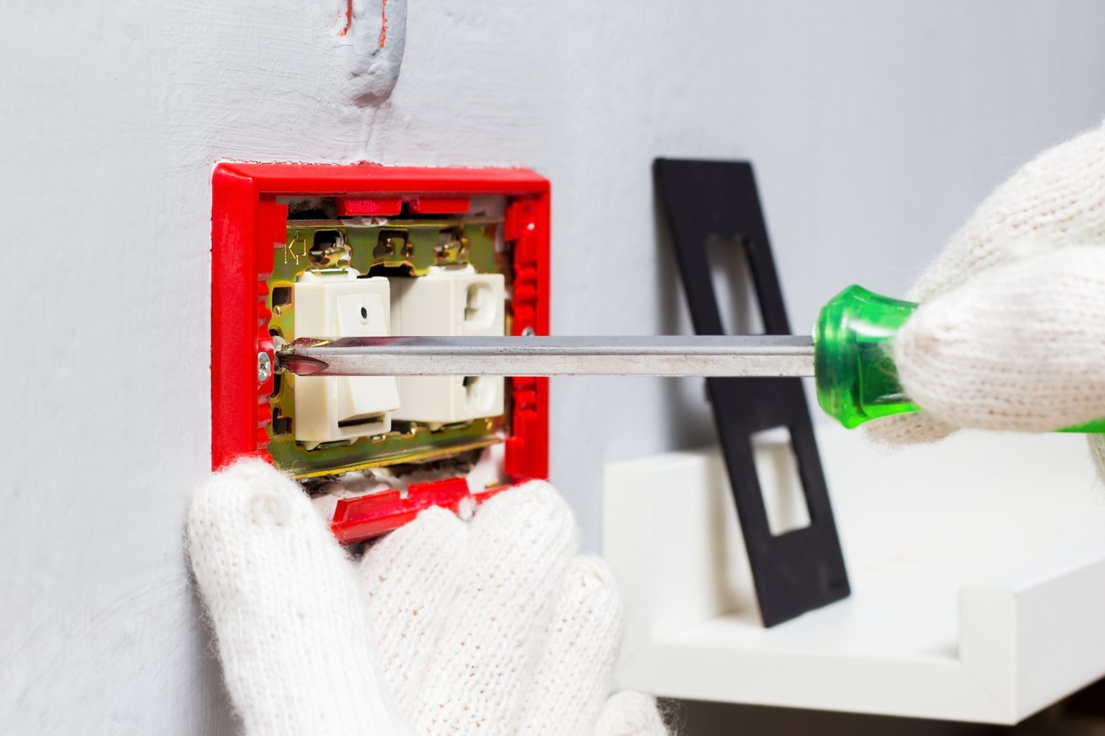 Person wearing gloves using a screwdriver on a red electrical panel, likely for maintenance.