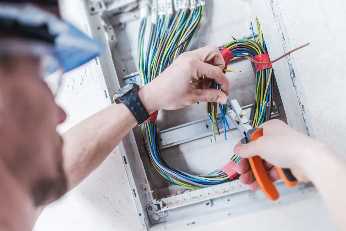 Electrician working on electrical wiring in a panel, using pliers.