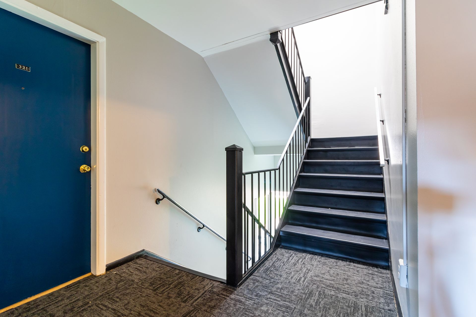 Blue door next to a carpeted staircase with a black railing leading upwards.