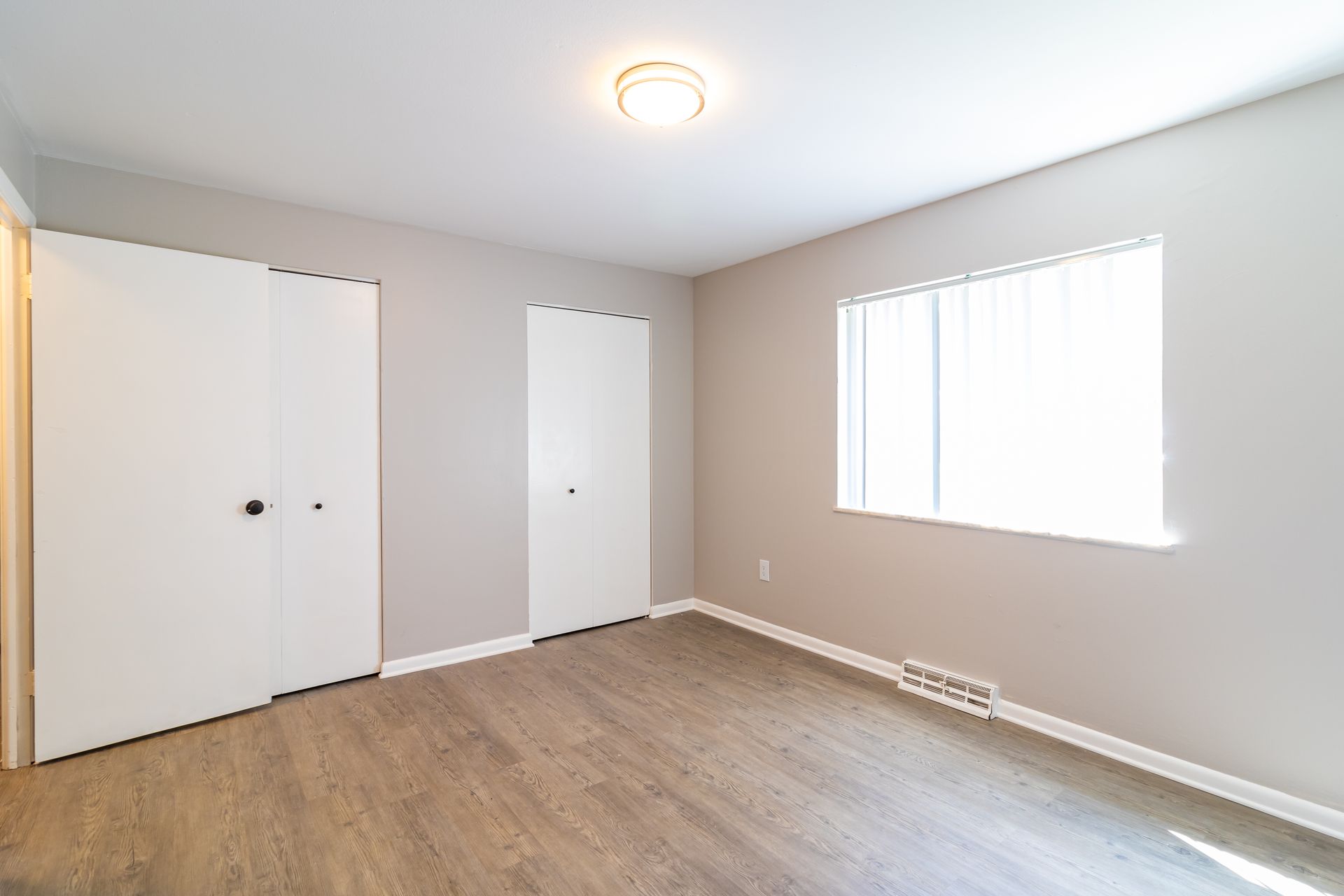 Empty bedroom with white doors, gray walls, and a window.
