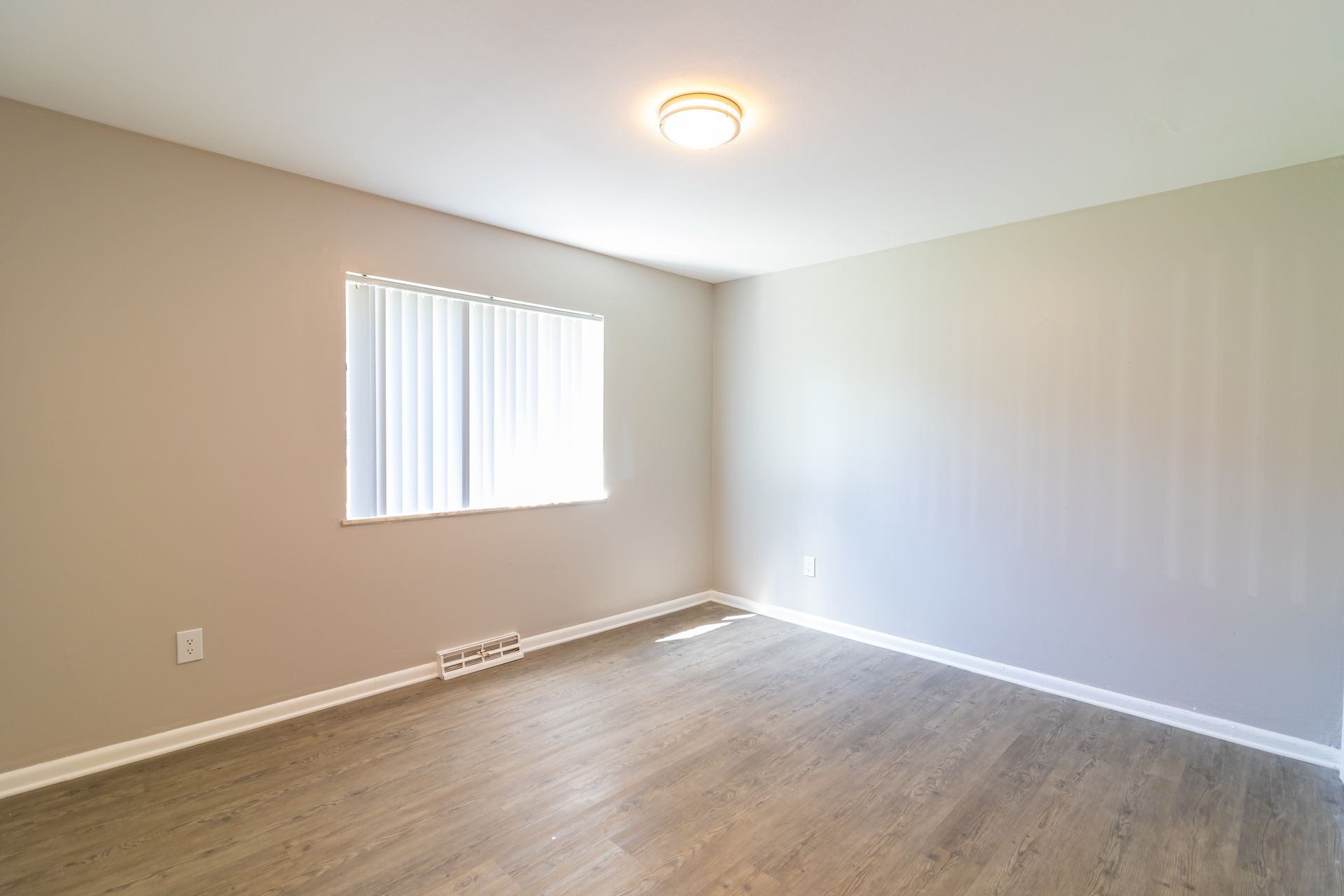 Empty bedroom with neutral-colored walls, window with blinds, and wood-look flooring.
