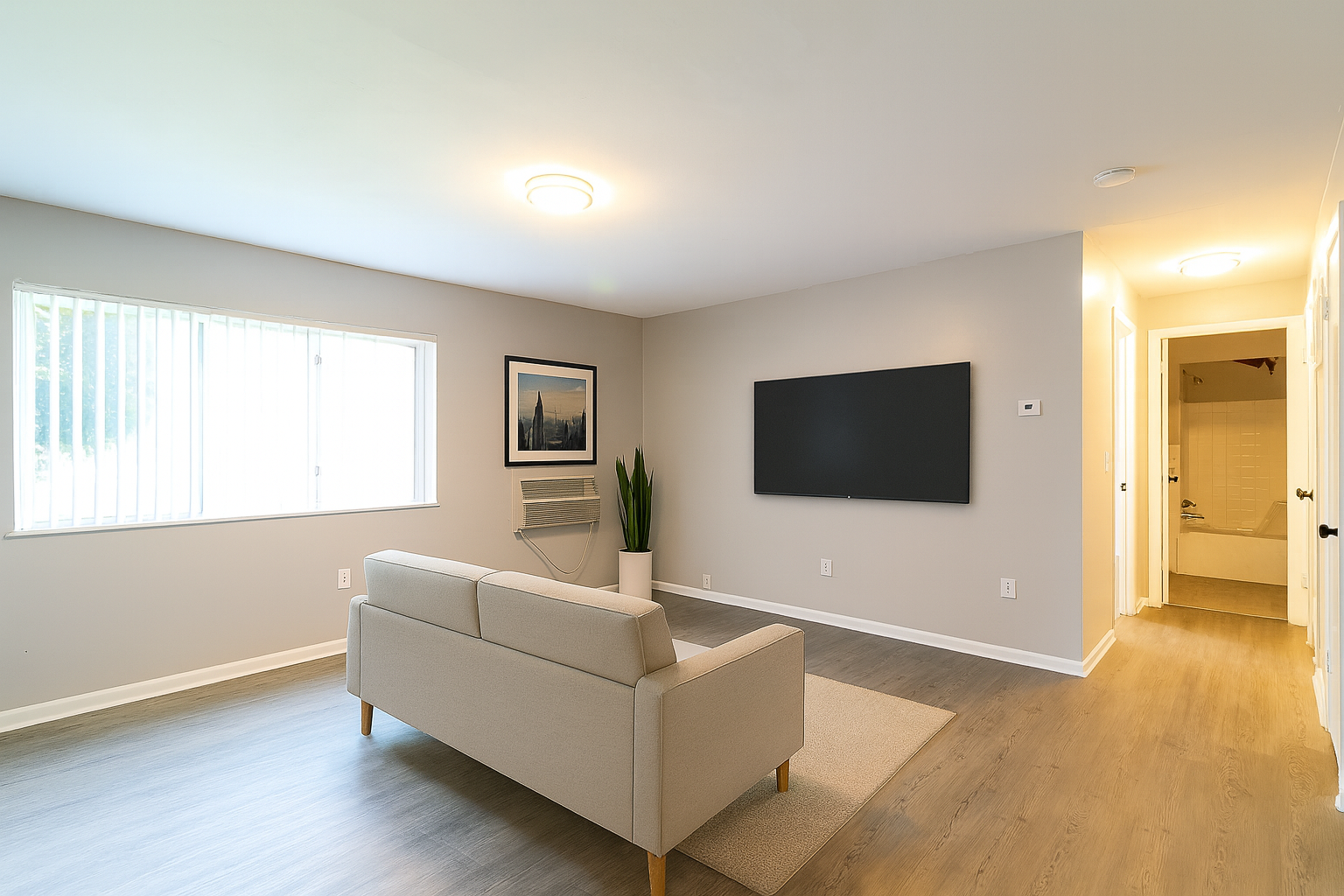 Living room with beige couch, large TV, and window.