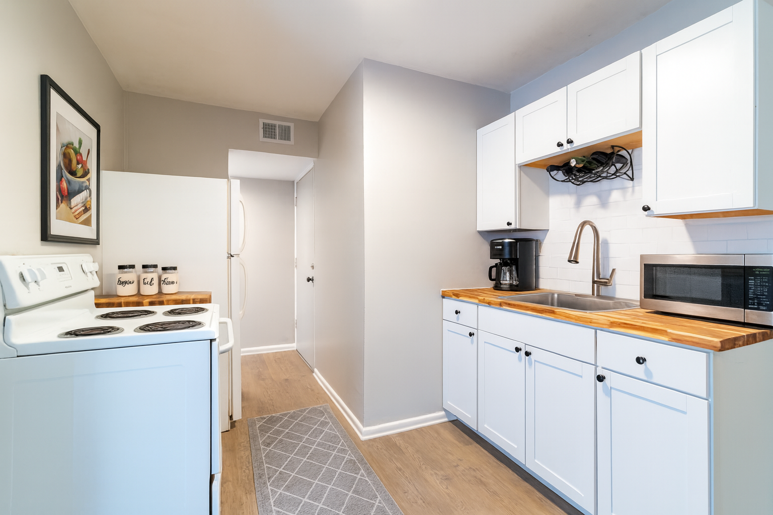 Small, renovated kitchen with white cabinets, stove, and appliances, wooden countertops, and a gray runner.