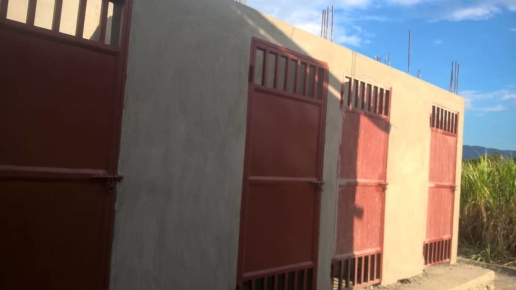 A row of three light-colored concrete structures with red metal doors and window grilles.