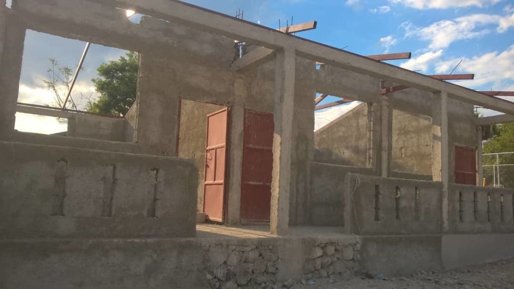 Partially constructed concrete building with open red doors and no roof.