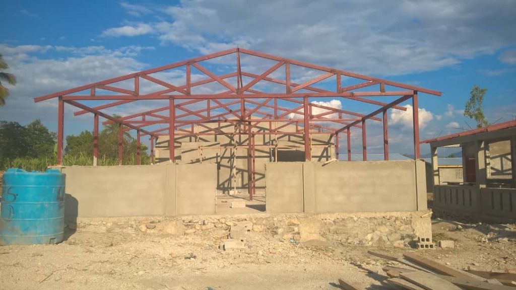 A construction site shows a building with a red steel frame and partial concrete walls.