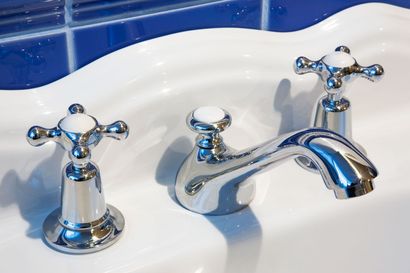 A chrome bathroom faucet with two cross-shaped handles mounted on a white sink against a blue tiled wall.