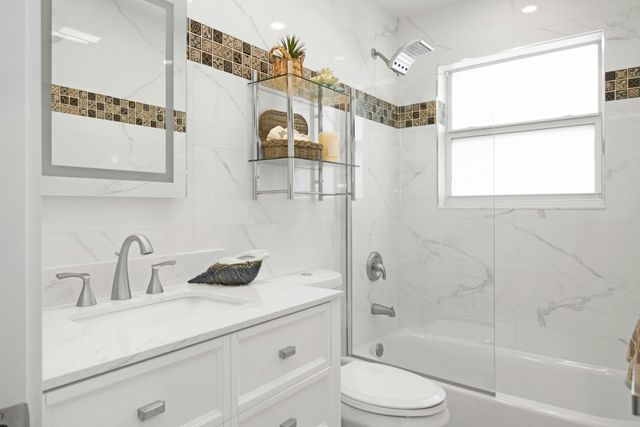 Modern bathroom with white marble-look walls, a white vanity, a glass shower enclosure, and a decorative tile accent band.