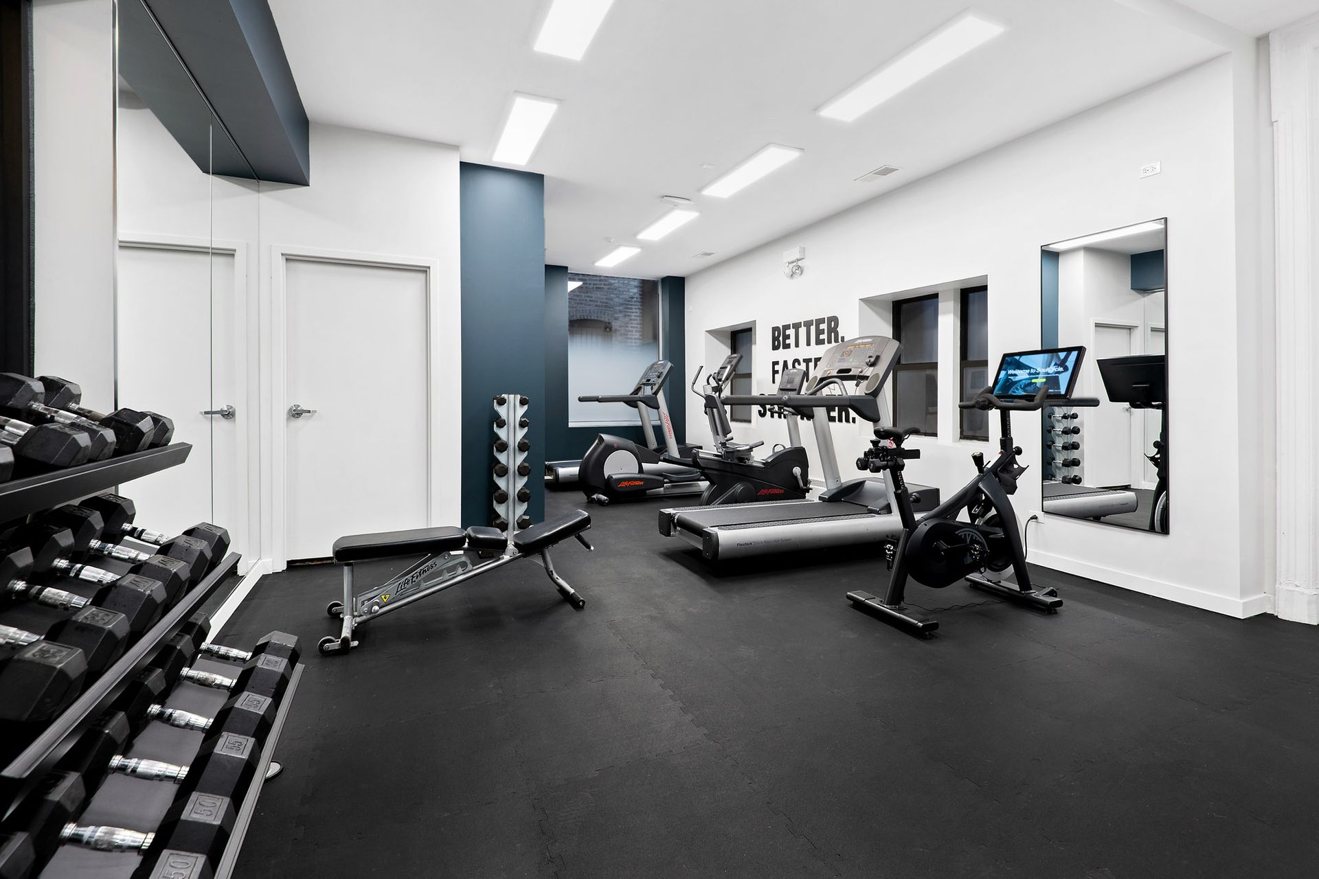 A gym with a treadmill, bicycle, dumbbells, and a mirror at Reside at Belmont Harbor. 
