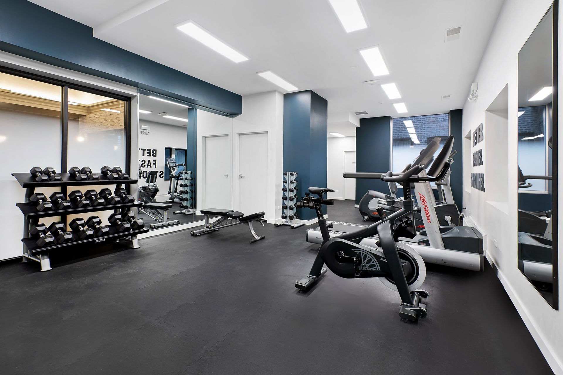 A gym with a bicycle, treadmill, dumbbells, and mirrors at Reside at Belmont Harbor. 