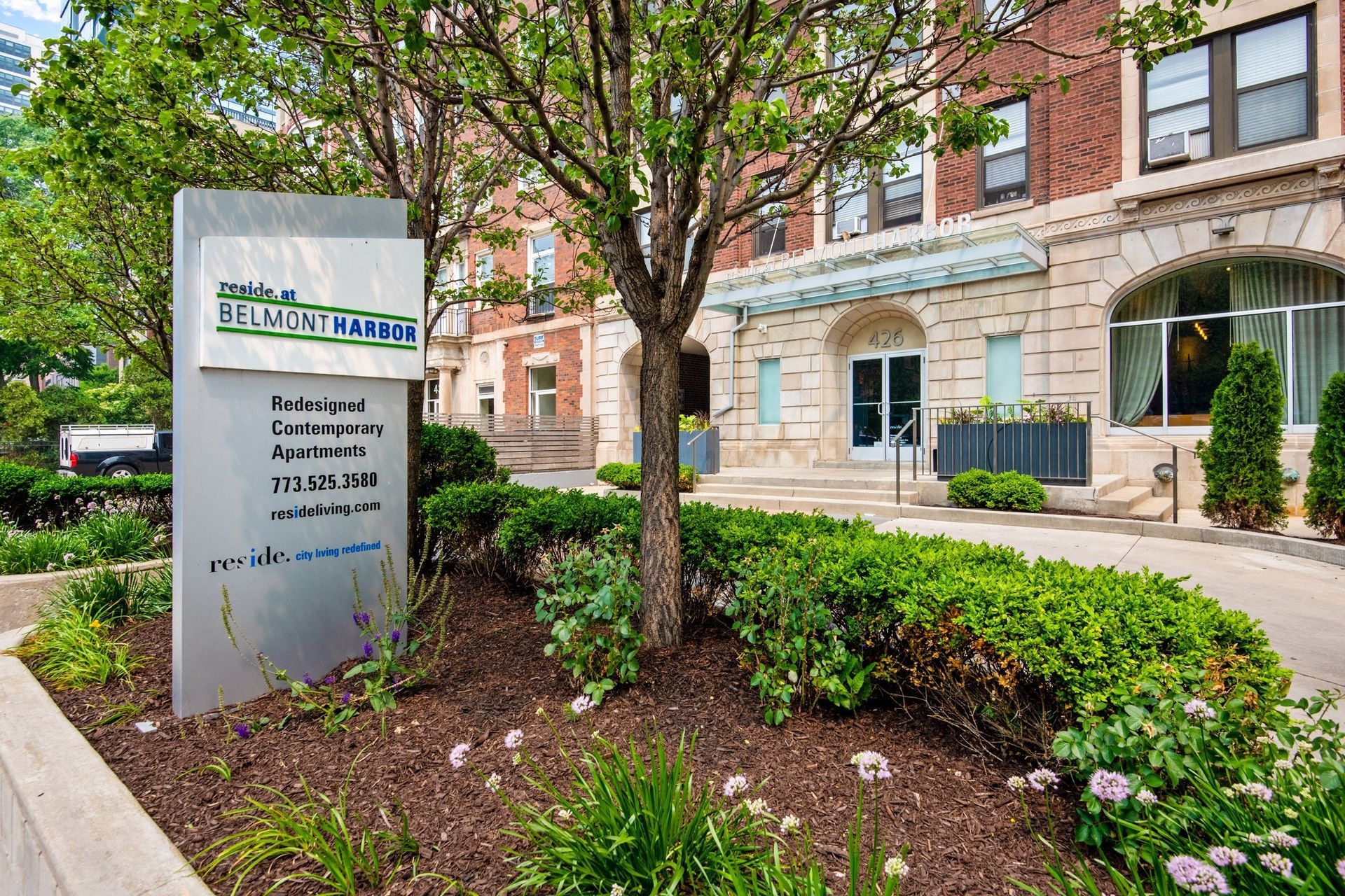 a sign in front of a building with a tree and plants