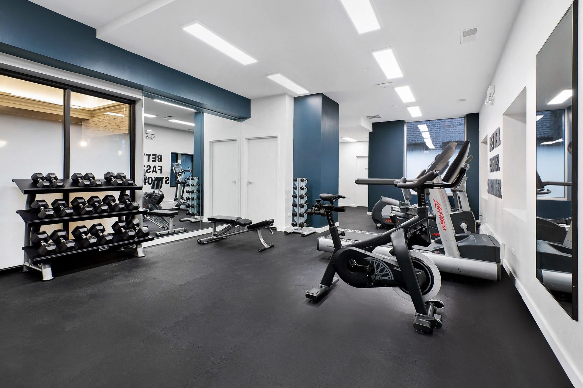 a gym with treadmills and weights on the floor and a wall of mirrors