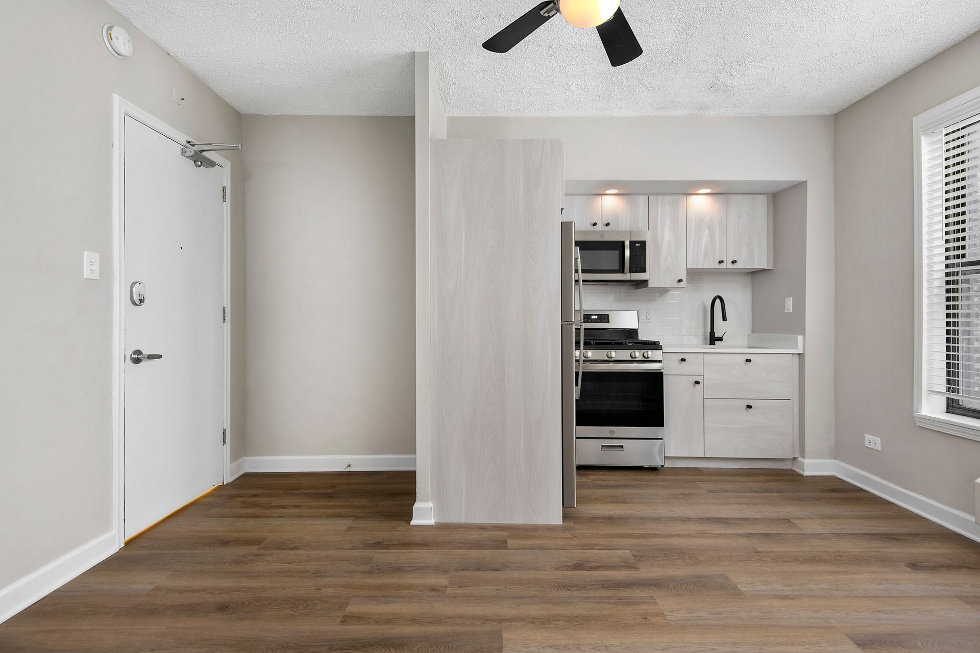 An empty apartment with a kitchen and a ceiling fan at Reside at Belmont Harbor. 