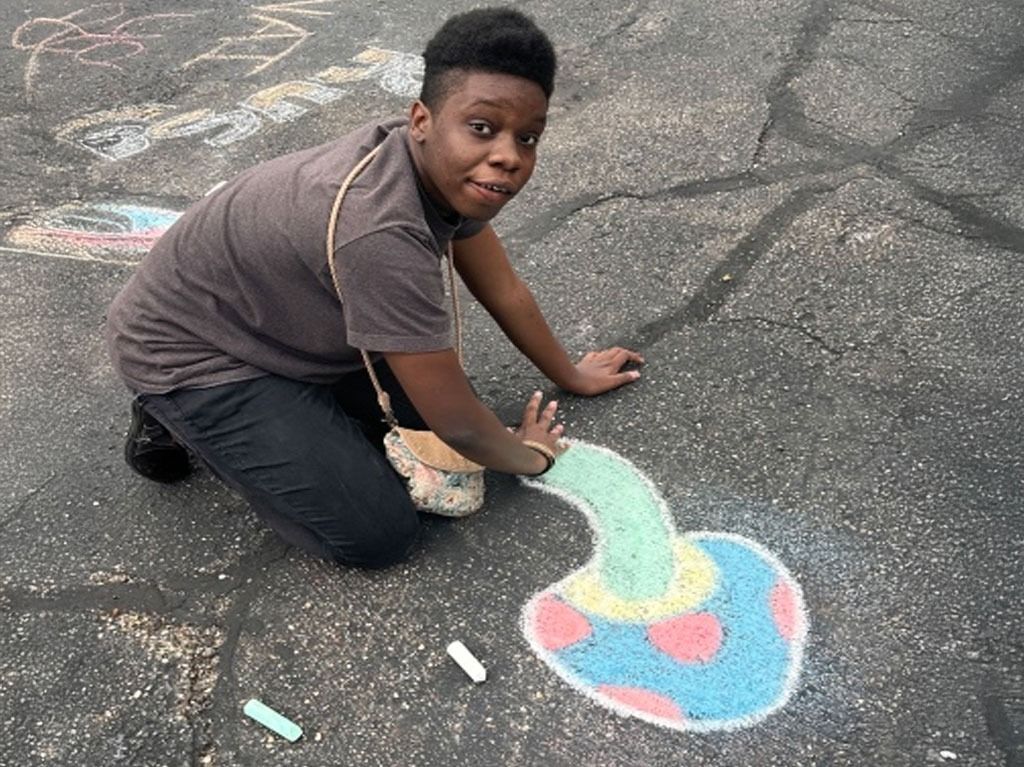 A person kneels to draw a colorful mushroom with chalk on asphalt.