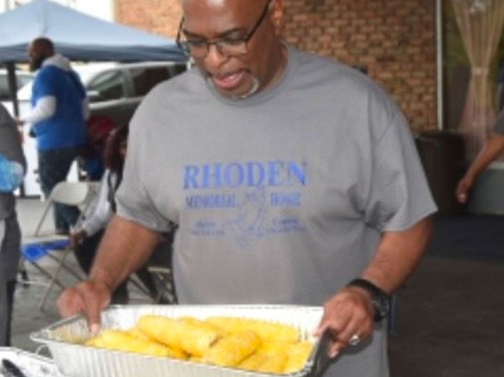 Man in glasses holds pan of corn, wearing a gray
