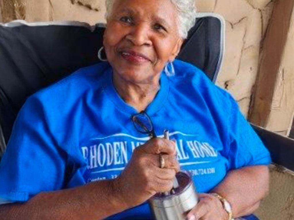 Elderly woman in blue shirt with silver container, smiling, outdoors.