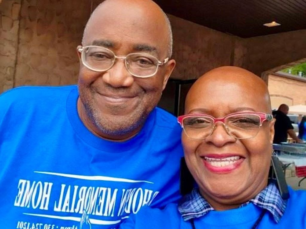 Two smiling people, likely a couple, in blue shirts and glasses, outdoors.