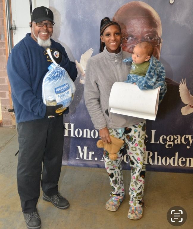 Man in blue, woman, baby, holding turkey, paper towels; event backdrop.