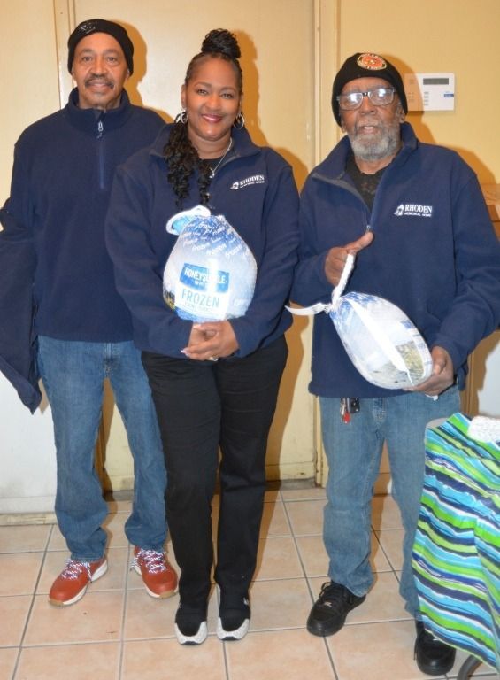 Three people wearing matching blue jackets, holding turkeys, standing indoors.