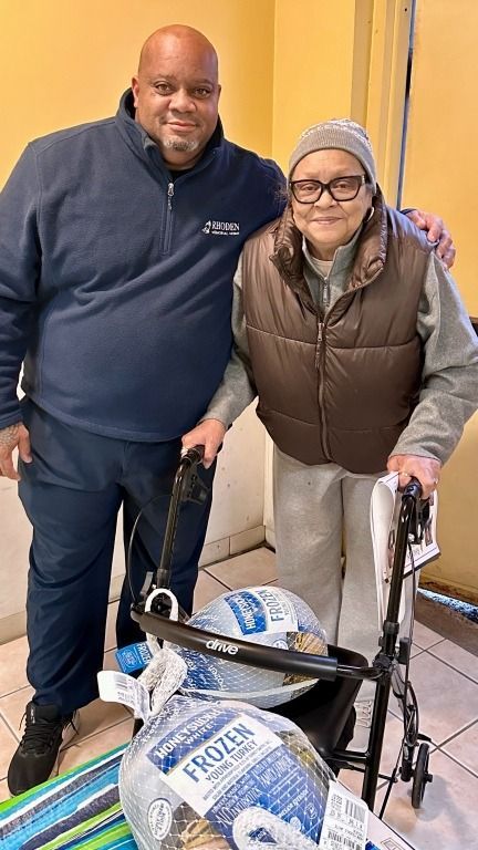 Man and woman pose with turkeys; woman uses a walker. Indoors, the man has arm around woman.