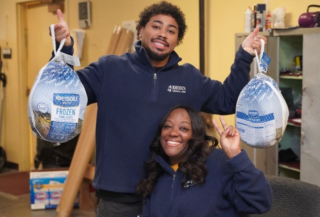 Two people holding turkeys; smiling in a room, man giving thumbs up, woman giving peace sign.