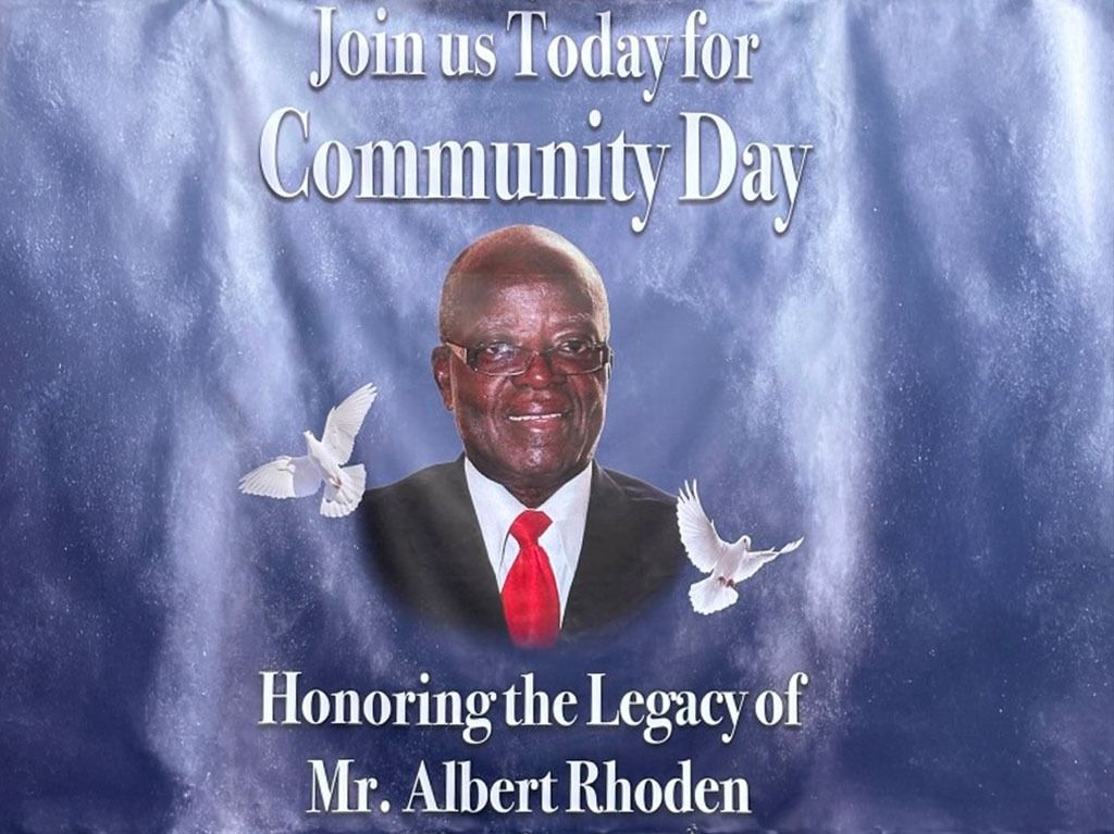 Community Day banner honoring Mr. Albert Rhoden, featuring his portrait, doves, and text on a blue background.