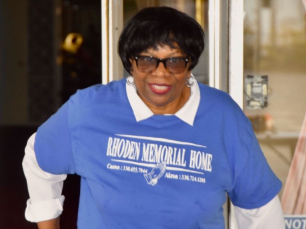 Woman in blue Rhoden Memorial Home shirt and sunglasses smiles.