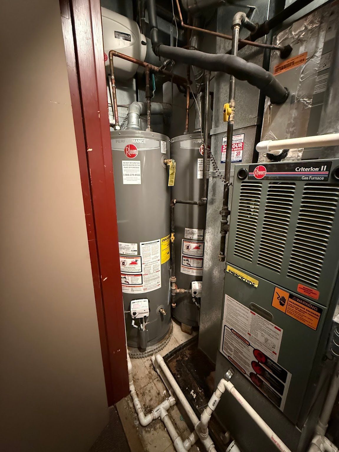 HVAC closet with gray water heaters, pipes, and a furnace unit in a narrow utility space