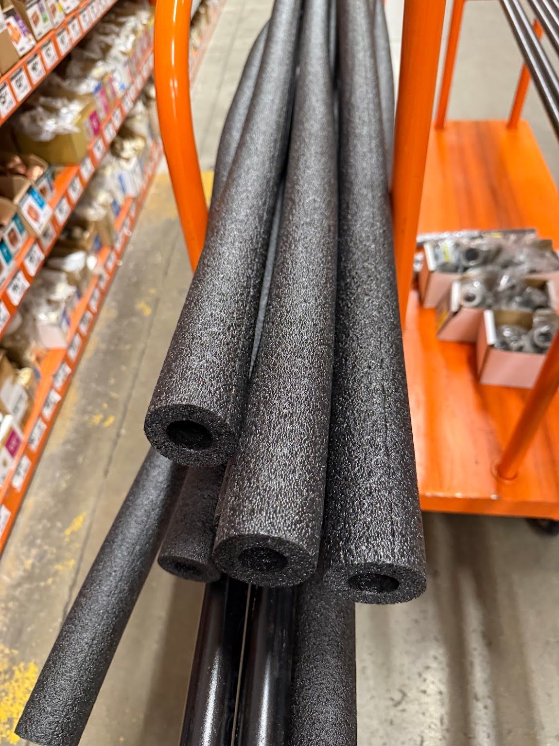 Foam pipe insulation tubes stacked on an orange cart in a hardware store aisle
