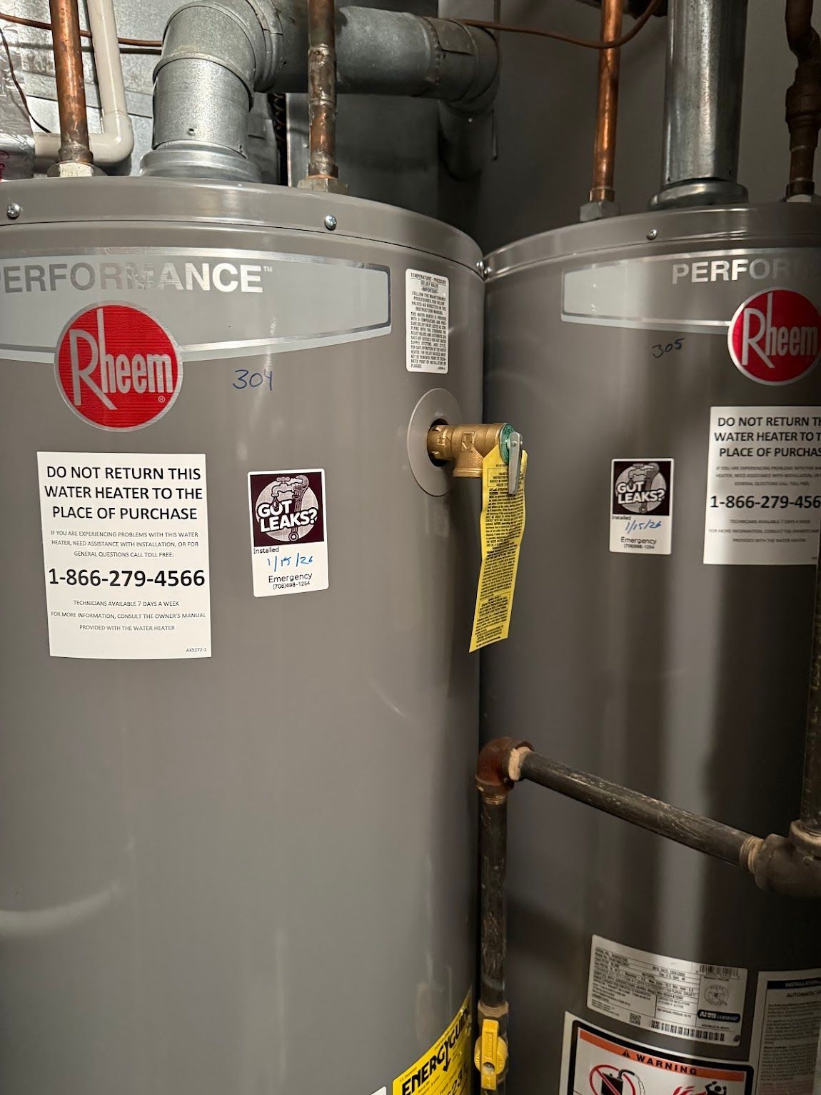 Two gray Rheem water heaters in a utility room, with pipes and valves visible.